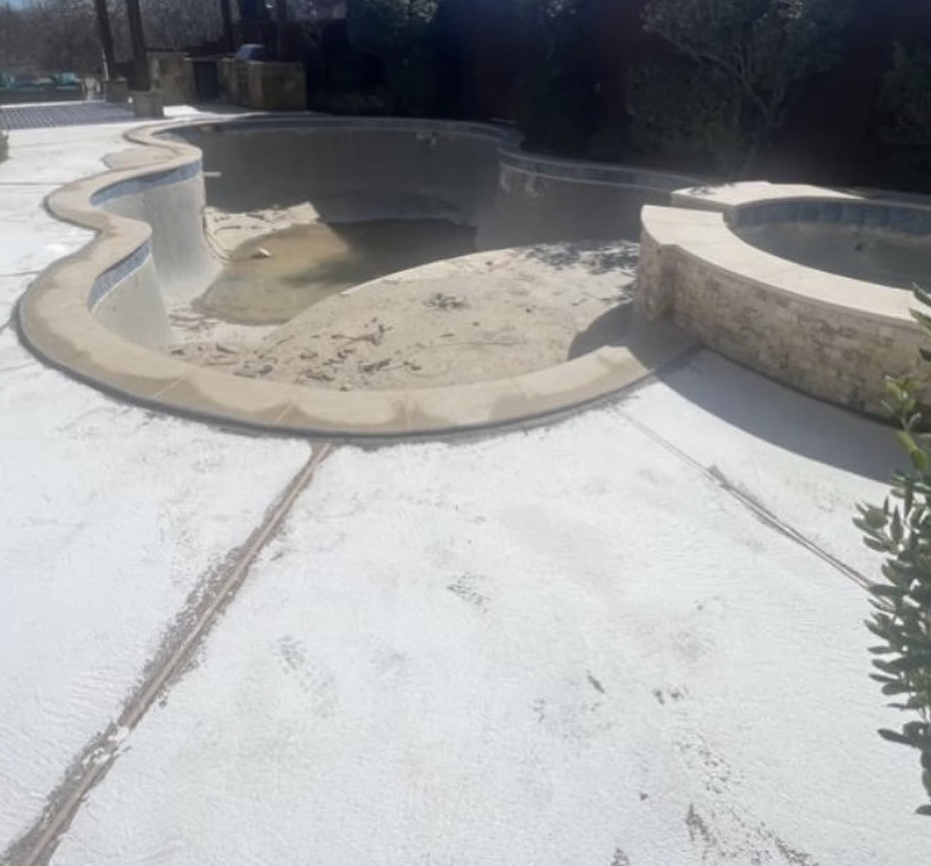 Before deck recoating: worn concrete around a drained pool and raised spa