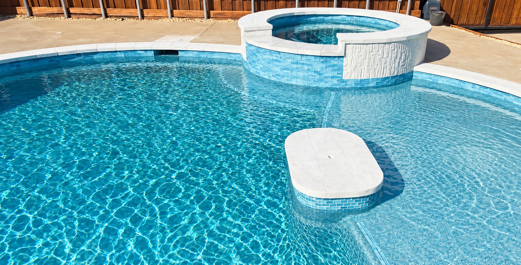 Pool finish beneath clear blue water, with a raised spa and shallow sun shelf