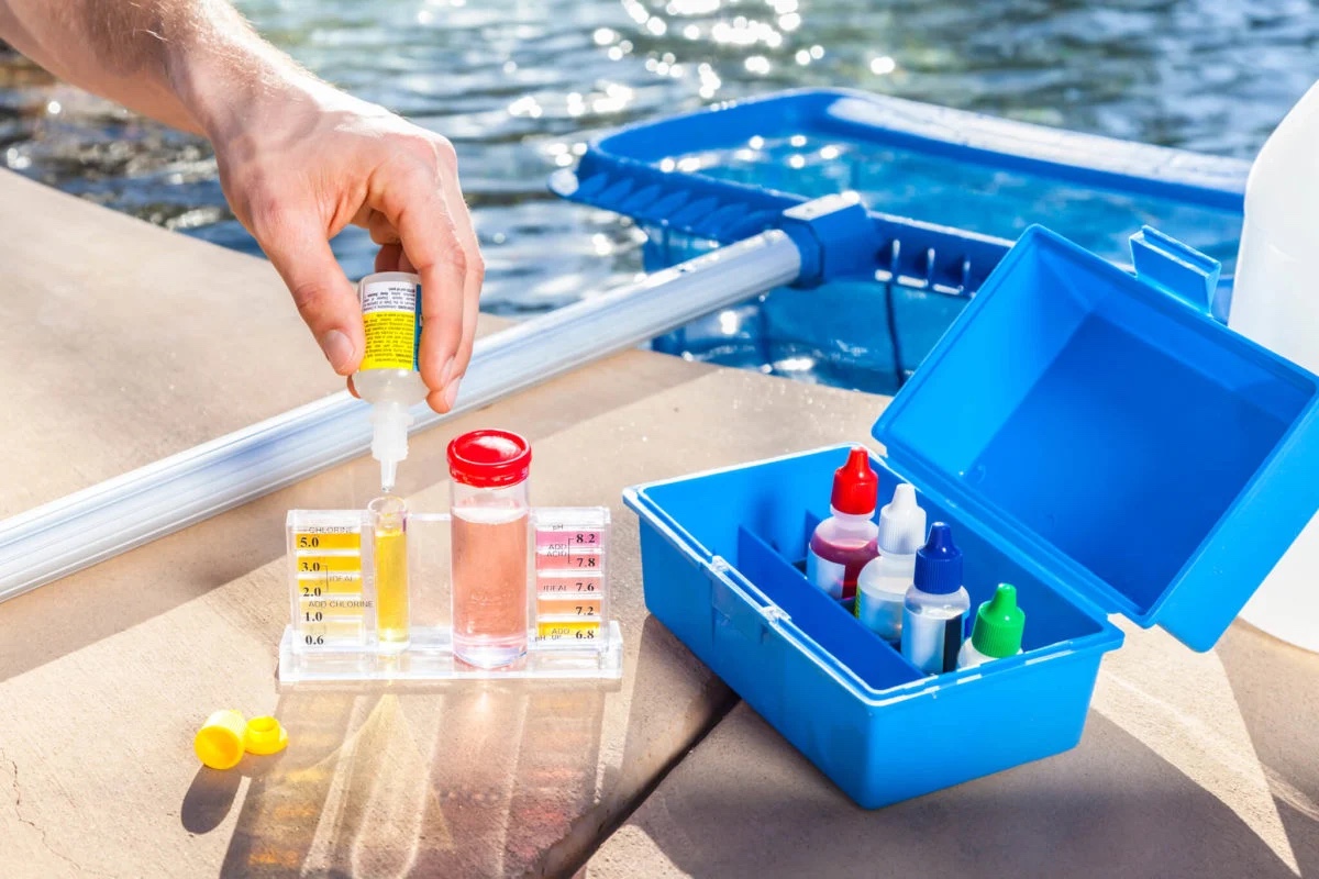 Pool water sample being tested beside a skimmer and service kit